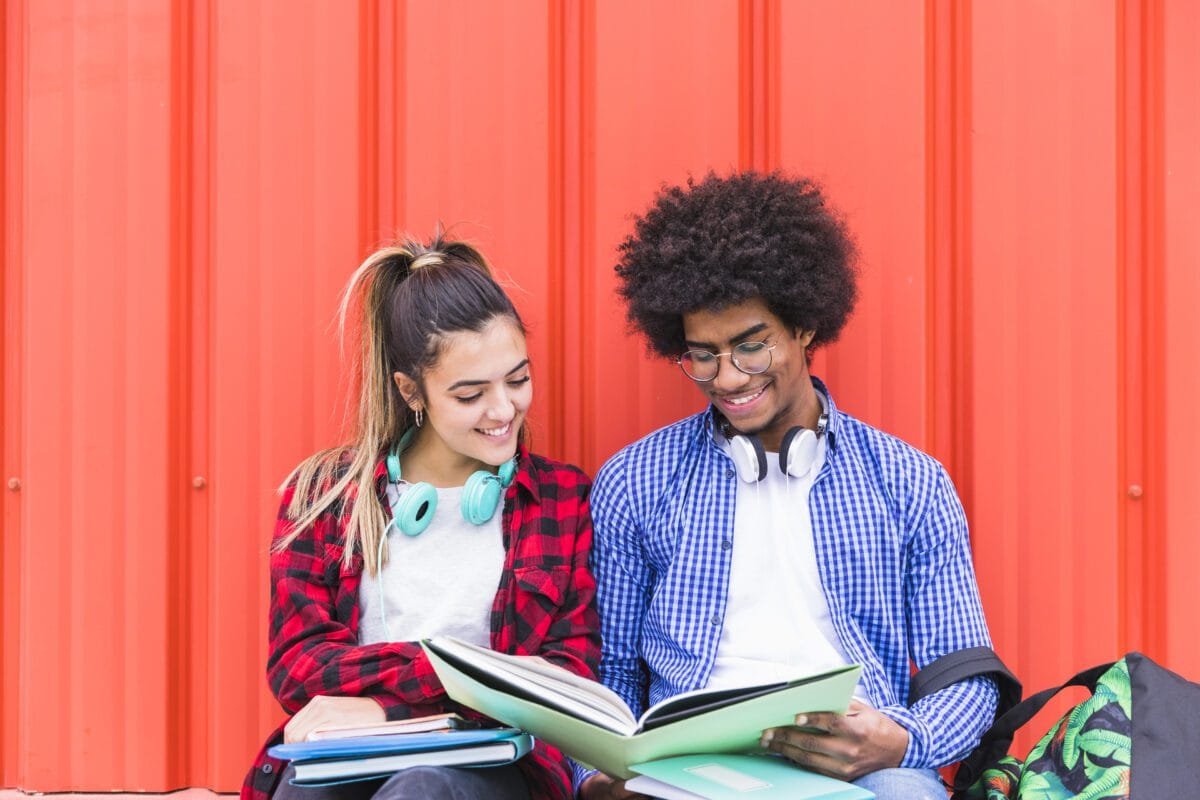 Casal de Estudantes lendo um livro em fundo laranja Desperta Debora