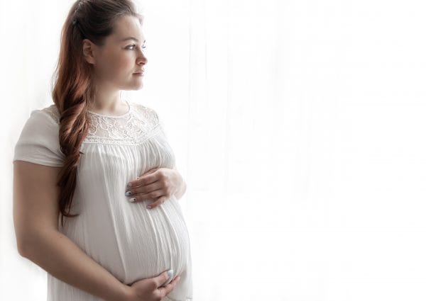 a young pregnant woman in a white t shirt looks thoughtfully out the window