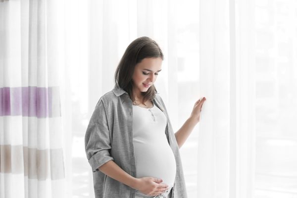 beautiful pregnant woman standing near window at home