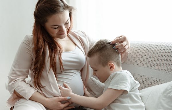 child boy hugging the belly of pregnant her mother on the couch at home