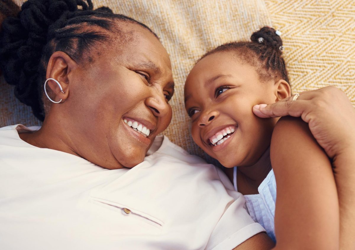 happy smile and family of a black grandma and child in happiness relaxing and lying on a bed at home senior african grandmother and little girl in joyful love and smiling together in the be