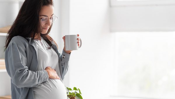 side view of pregnant woman at home with mug of coffee