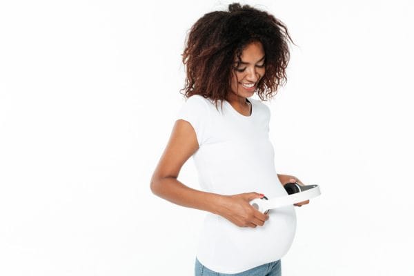 smiling young pregnant african woman listening music with headphones