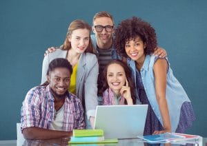 Happy classmates using laptop on table