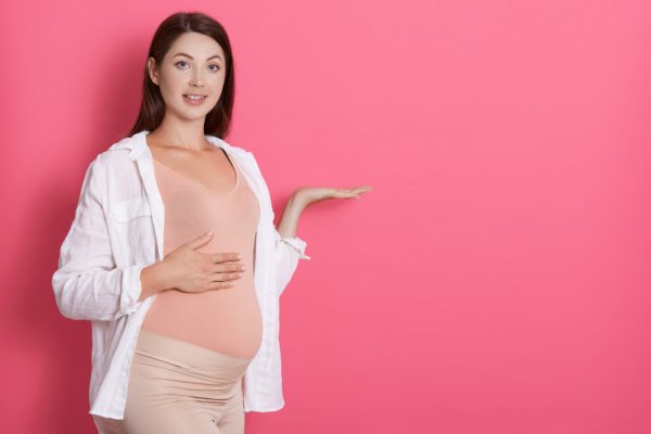 young beautiful pregnant girl expecting baby isolated over pink space pointing aside with hands open palms showing copy space presenting advertisement looks smiling at camera 1