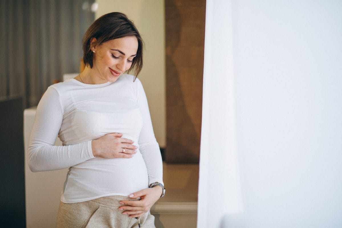 young pregnant woman standing by the window at home