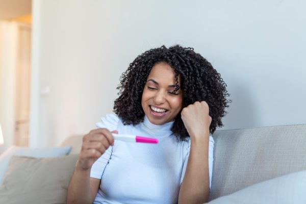 young woman looking at pregnance test in happiness finally pregnant attractive black women looking at pregnancy test and smiling while sitting on the sofa at home 1